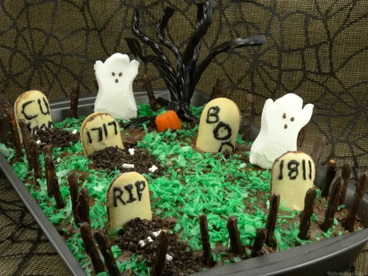 close up image of a haunted graveyard Halloween cake with marshmallow ghosts, tombstones, and a rickety fence