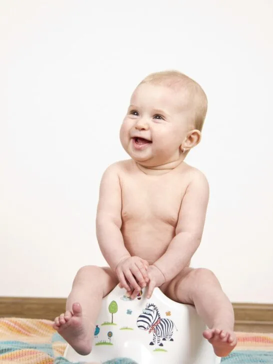 A baby sitting on a training potty smiling