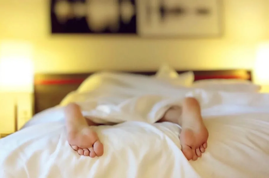 two feet peeking out of the sheets while a person is sleeping on a bed