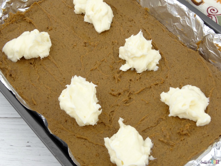 top Pumpkin Spice Bars batter with large spoonfuls of cream cheese frosting