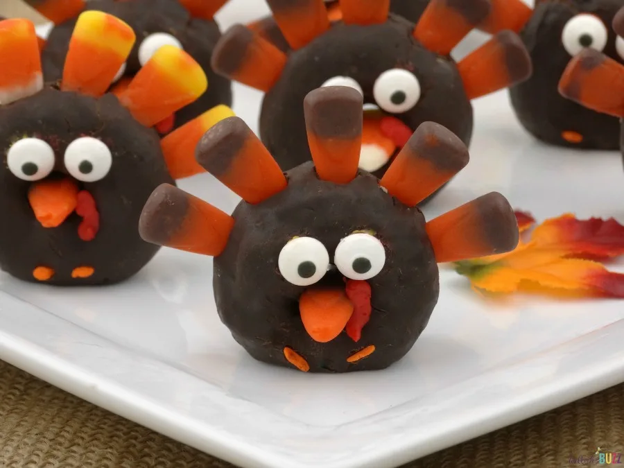 Mini turkey donuts with candy corn feathers lined up on a white plate.