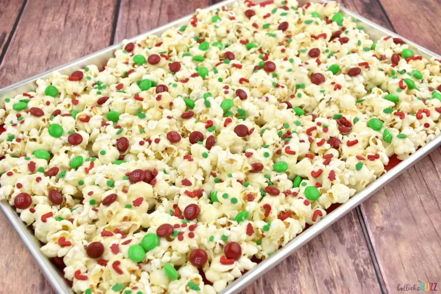 Adding Christmas colored sprinkles to the layer of popcorn on the cookie sheet.