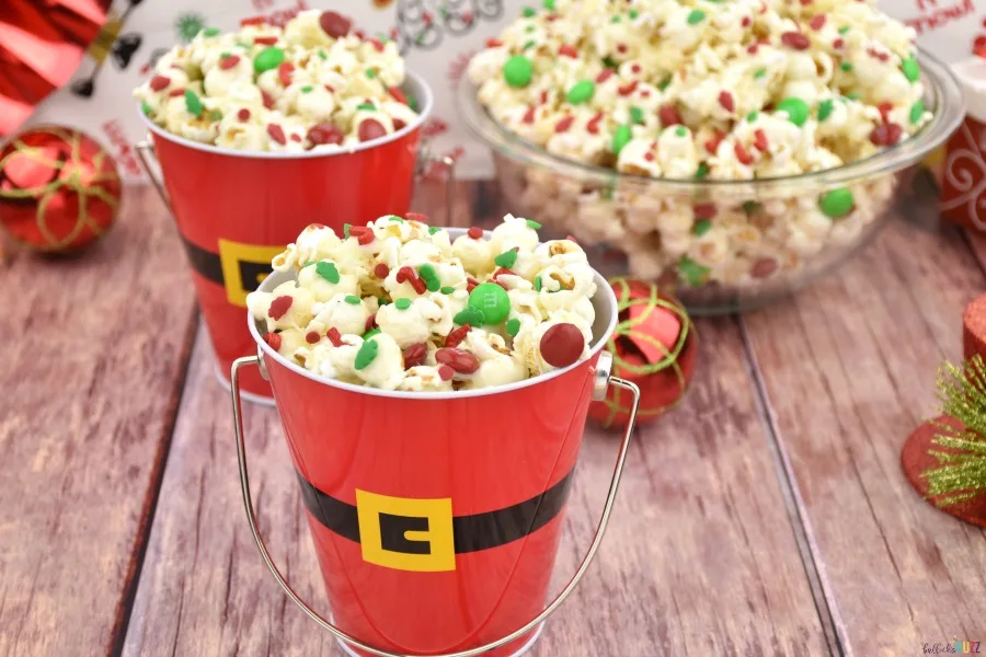 Christmas popcorn served in Santa pails and in front of a bowl of the same popcorn