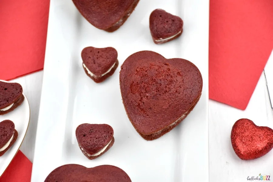 Close up image of small and large heart-shaped red velvet whoopie pies on white plate
