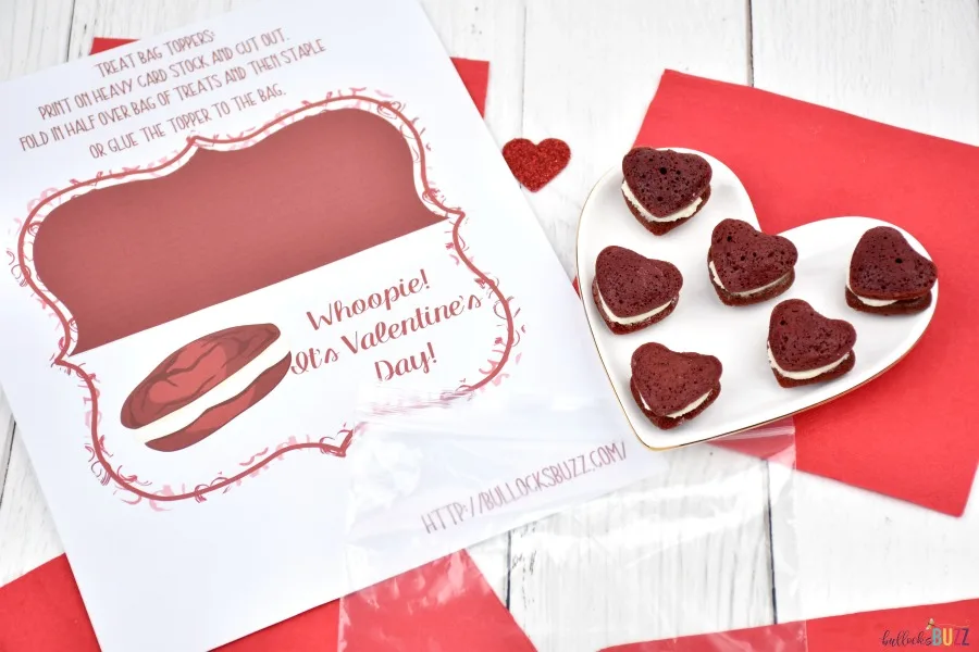 Image of the printed out treat bag topper printable with an empty plastic bag and a plate of mini heart-shaped red velvet whoopie pies for a Valentine's Day treat