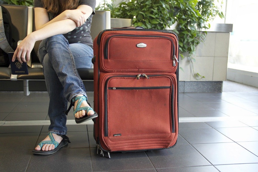 woman sitting next to an orange suitcase to pack for an asian vacation