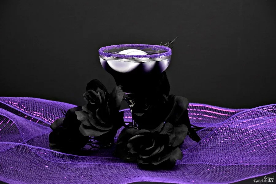 Halloween cocktail in glass surrounded by black roses