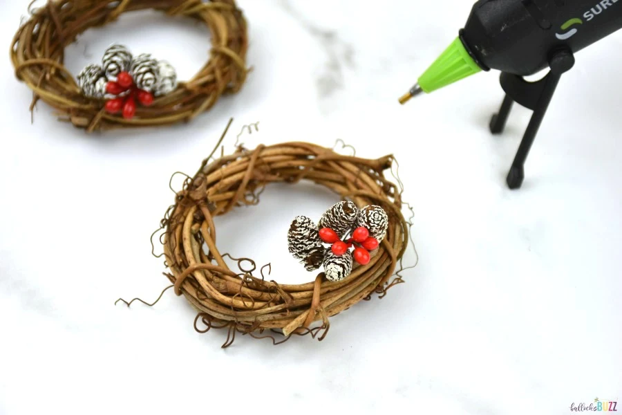 use hot glue to attach pinecone and berry picks to wreath