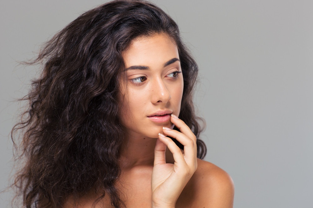 Beauty portrait of a lovely woman with fresh skin from perfecting your skincare routine looking away over gray background