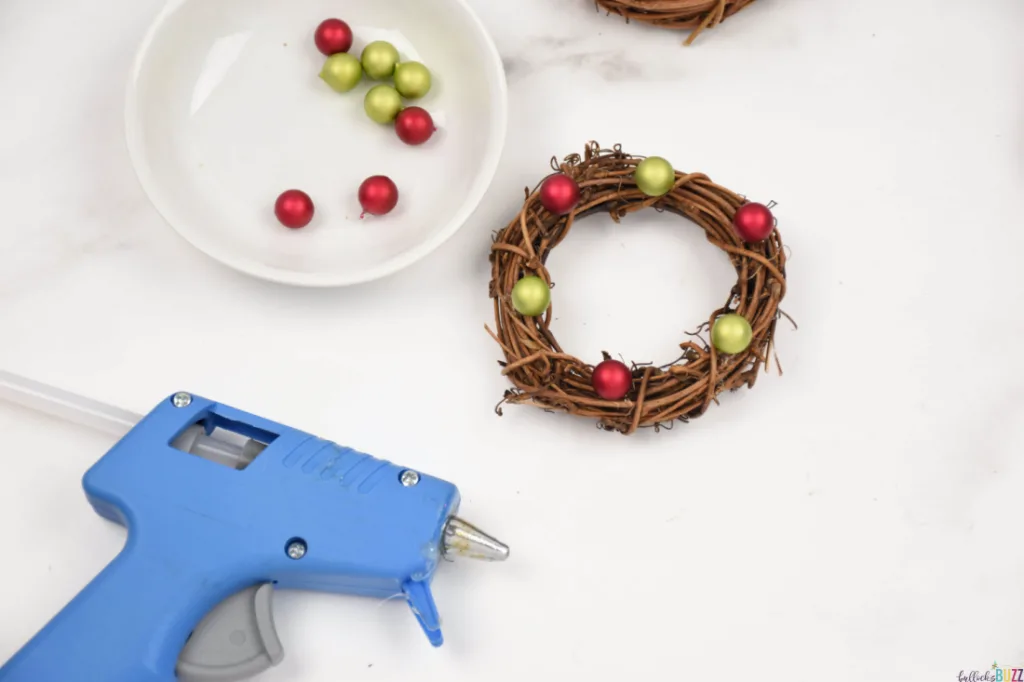 Adding berries to a mini wreath form using hot glue