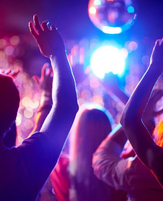Crowd of people with raised arms dancing in night club while they visit Vegas