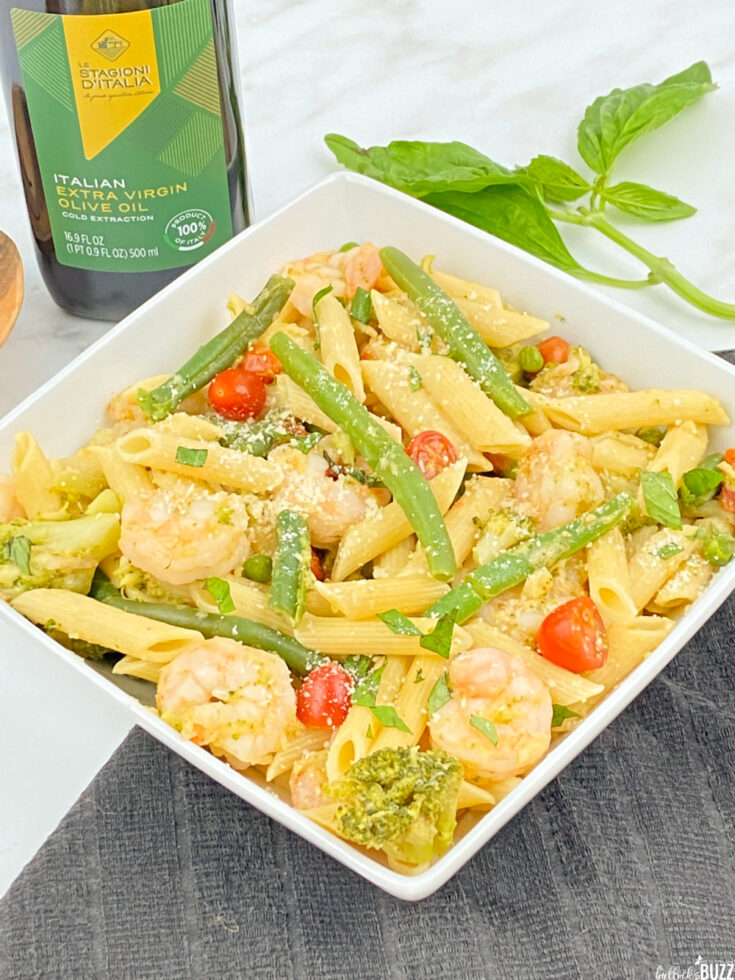 pasta primavera with shrimp in bowl in front of bottle of olive oil