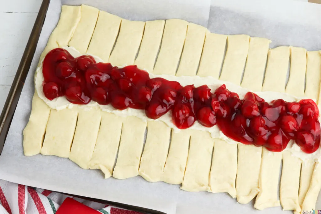 spread cream cheese and cherries on top of dough for Cherry Danish