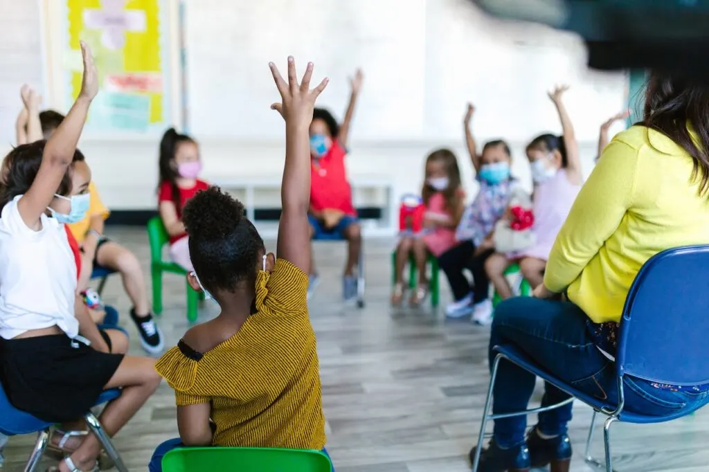 students sitting in circle with raisedhands