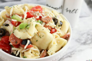 close up of tortellini pasta salad in a bowl sitting on a table