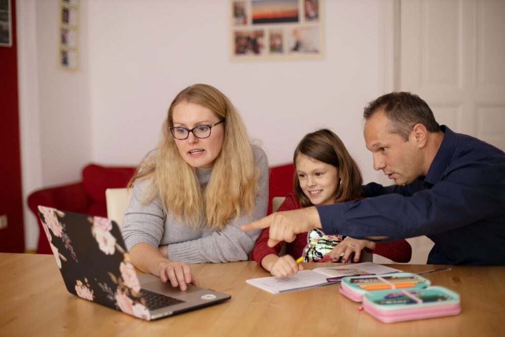 family sitting at table looking at laptop for ways to earn extra money from home