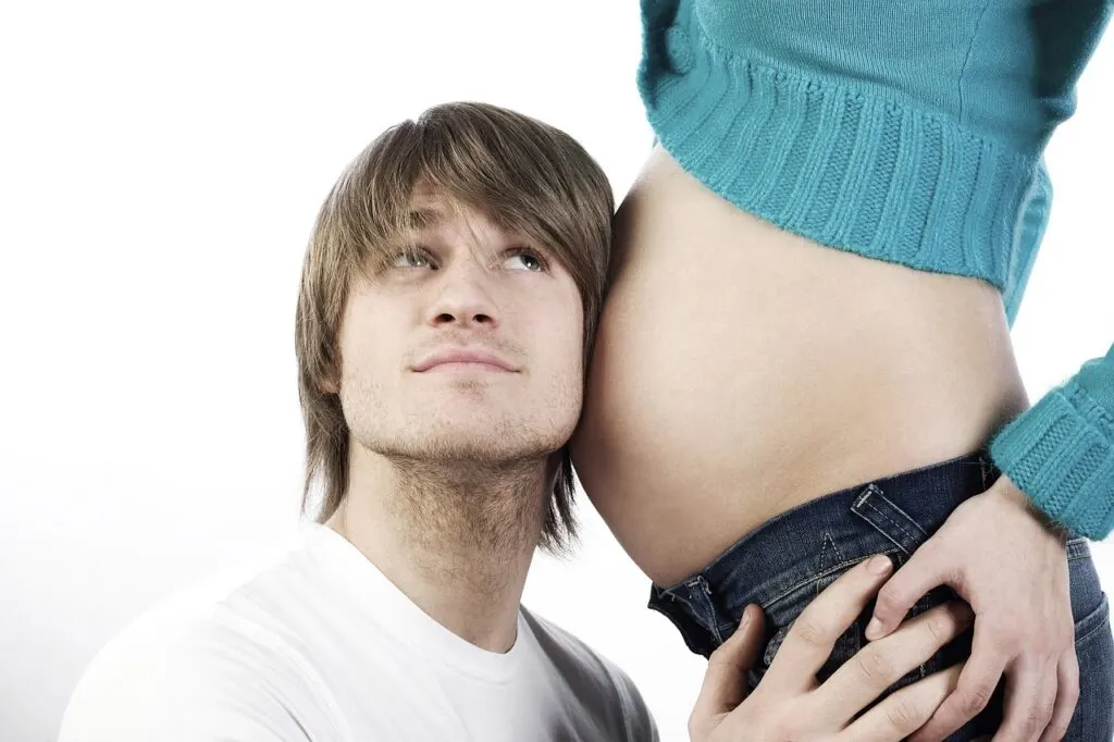 man with his ear against his wife's pregnant stomach listening to baby