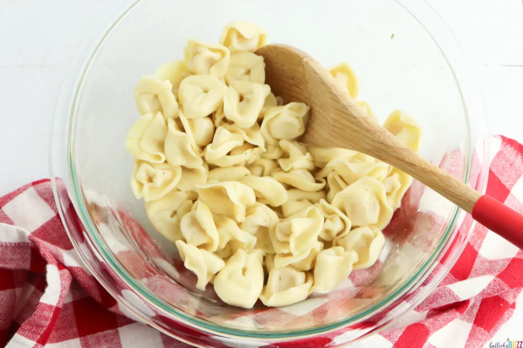 bowl of prepared tortellini pasta with wooden spoon 