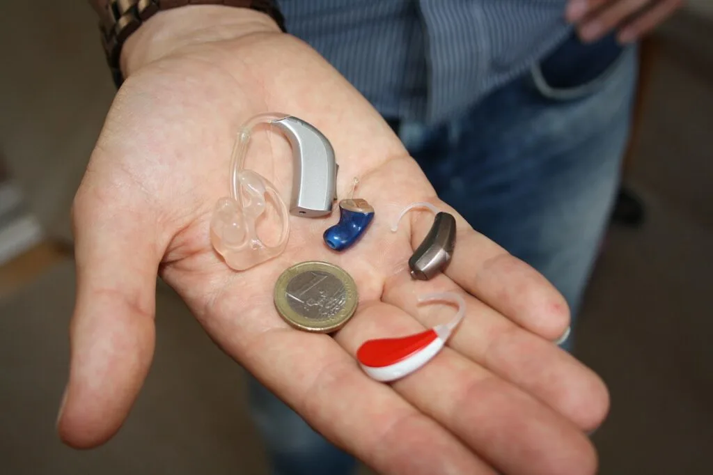 man holding several types of hearing aids in his hand next to a coin for size comparison when choosing the right hearing aid