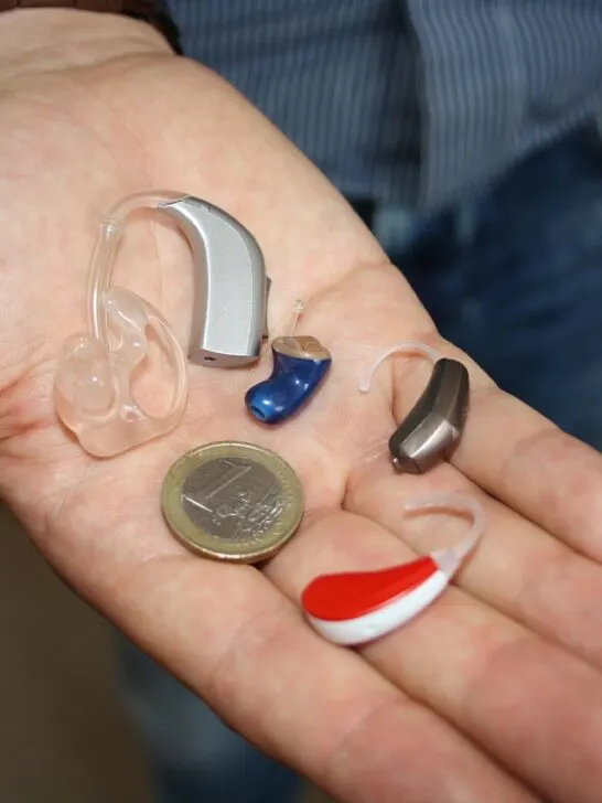 man holding several types of hearing aids in his hand next to a coin for size comparison when choosing the right hearing aid
