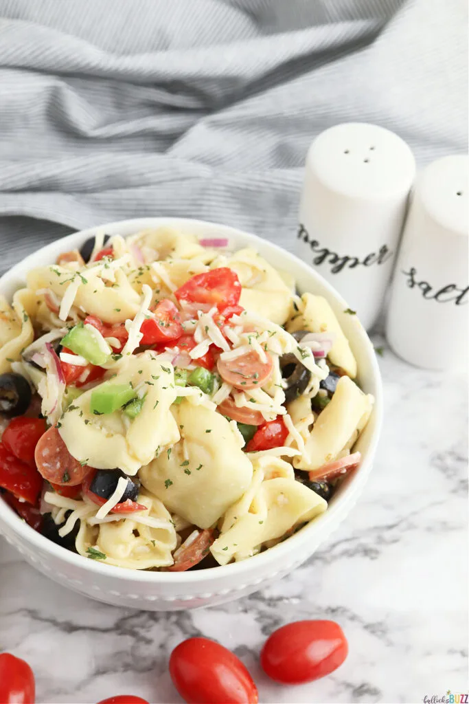 a bowl of Tortellini Pasta Salad is sitting in a white bowl next to salt and pepper shakers on a table