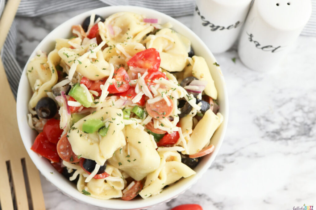 a bowl full of tortellini pasta salad sprinkled with parsley
