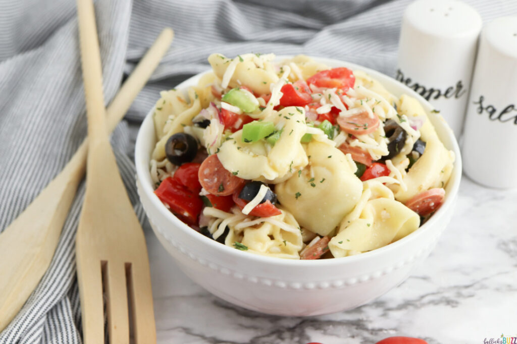 Tortellini Pasta Salad served in a white bowl with wooden utensils lying next to the bowl