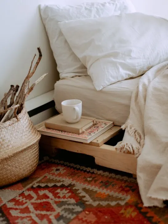 A natural wood bed with white sheets and a rug with warm colors. Using neutral and warm colors like these is just one of the diy tips to help you create a cozy bedroom you will love!