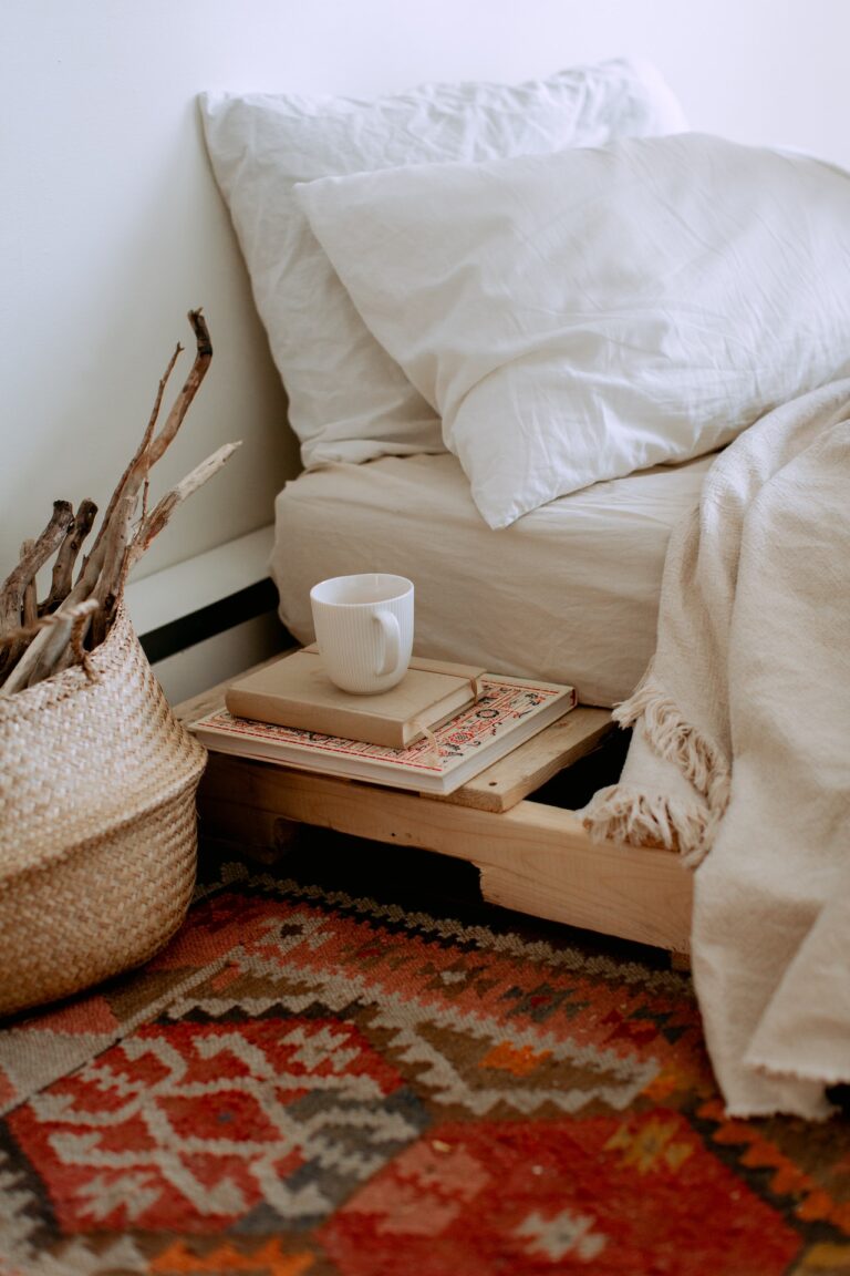 A natural wood bed with white sheets and a rug with warm colors. Using neutral and warm colors like these is just one of the diy tips to help you create a cozy bedroom you will love!