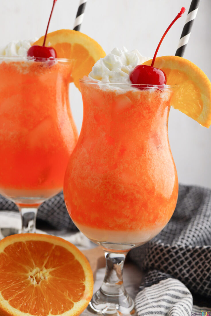 two Orange Creamsicle Mocktails in hurricane glasses garnished with whipped cream, orange slice, cherry, and a straw