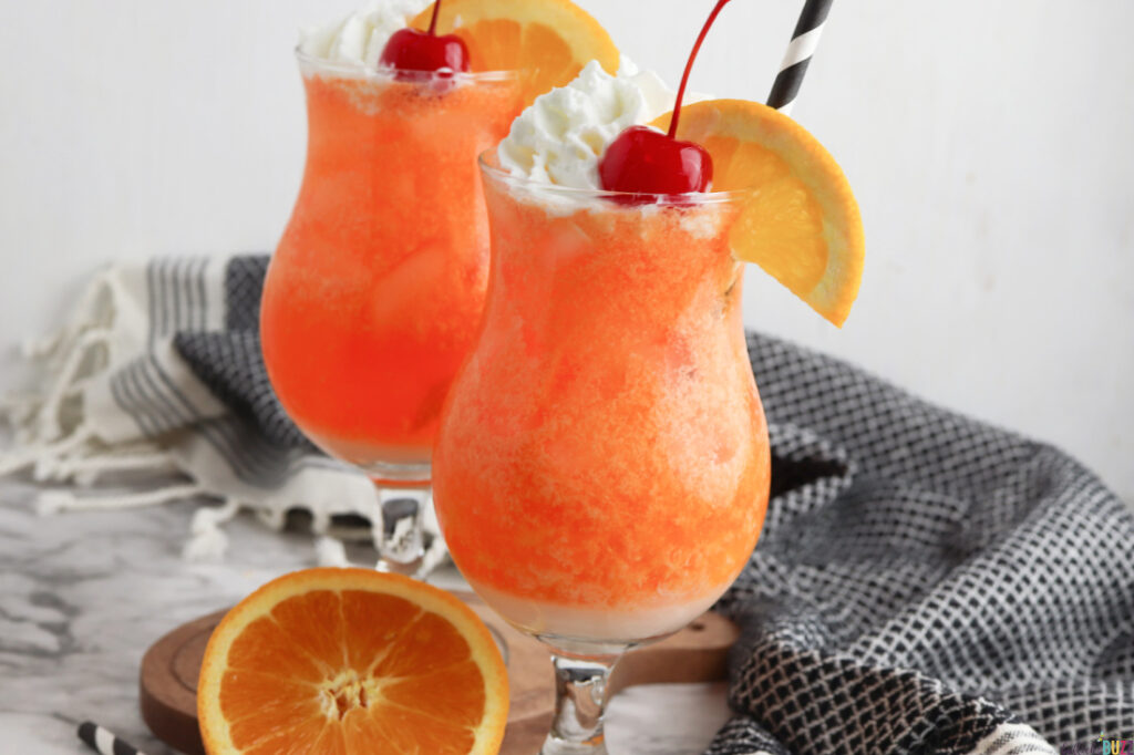 orange creamsicle mocktail garnished with orange wheel, whipped cream and a cherry, then finished off with a black and white straw