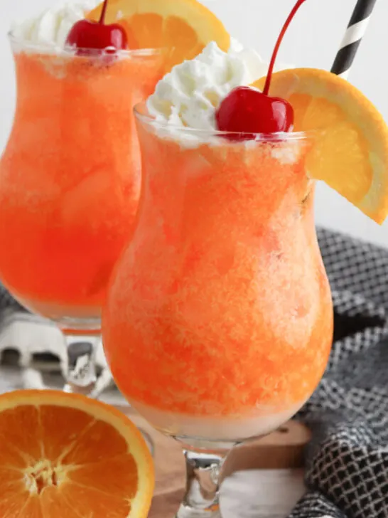 orange creamsicle mocktail garnished with orange wheel, whipped cream and a cherry, then finished off with a black and white straw