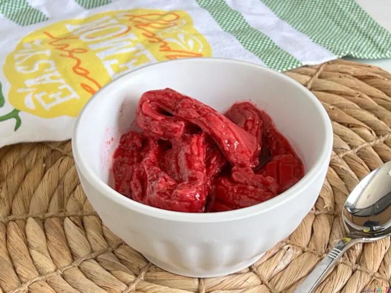 A white bowl full of homemade raspberry sorbet made in the Uber Appliance Sorbet Maker that is sitting on a rattan placemat with a spoon.