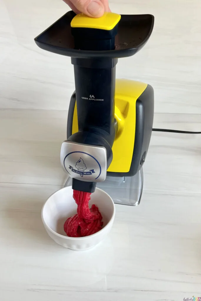 pushing down on the Uber Appliance Sorbet Maker while fresh raspberry sorbet comes out the spout