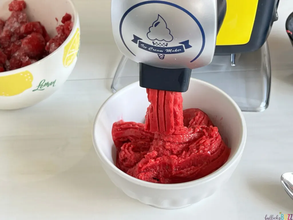 close up of homemade raspberry sorbet coming out of the spout of the sorbet maker and into a white bowl