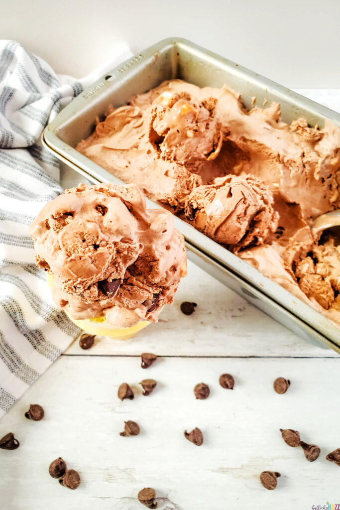 pan full of homemade rocky road ice cream next to a scoop of the ice cream on a cone surrounded by chocolate chips