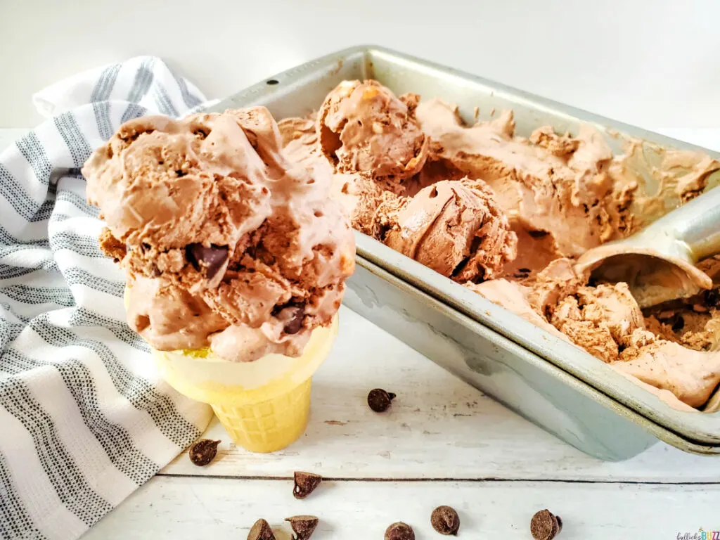 a scoop of homemade rocky road ice cream on a cone next to a pan filled with the ice cream