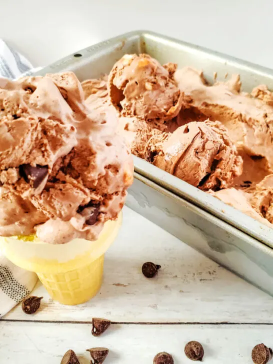 a scoop of homemade rocky road ice cream on a cone next to a pan filled with the ice cream