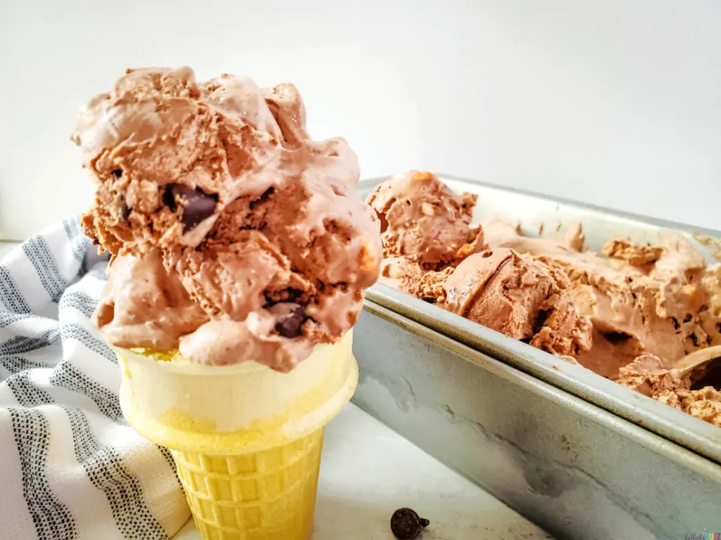 rocky road ice cream on a cone in front of a pan of the same ice cream