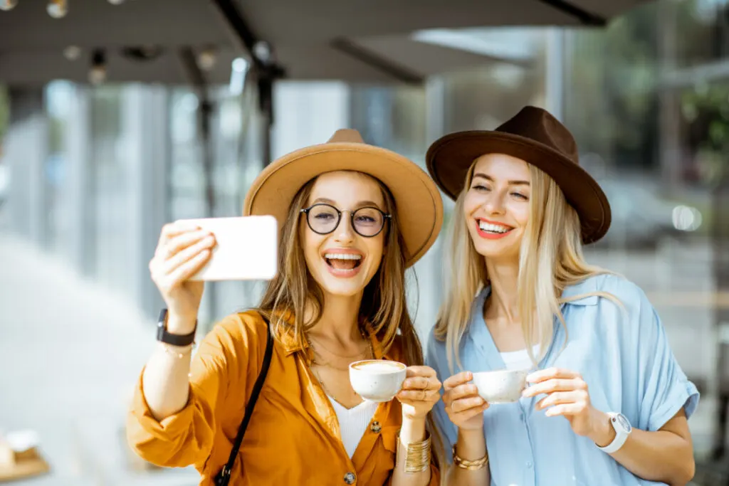 two women taking a selfie while holding coffee
