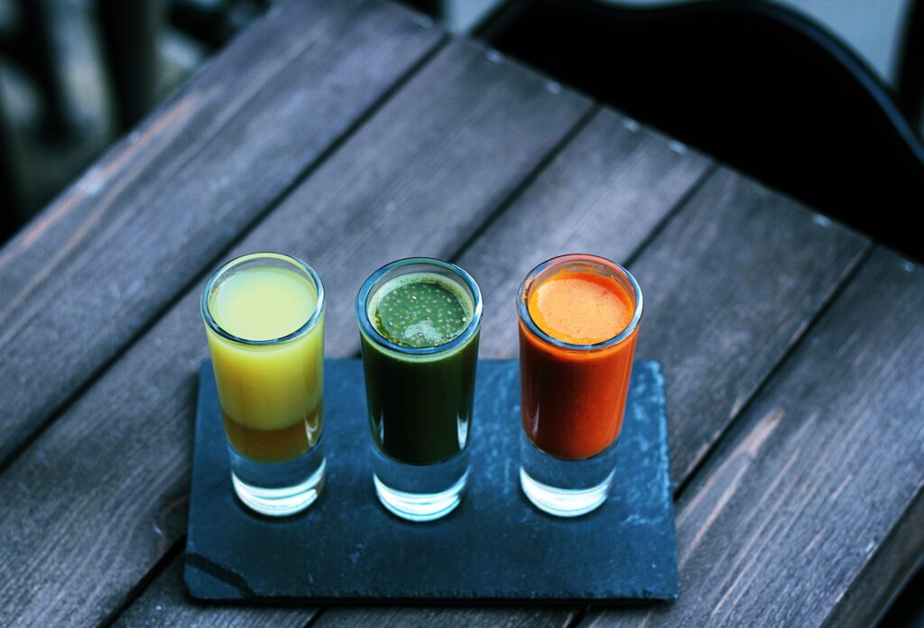 three shot glasses filled with different type of juice 