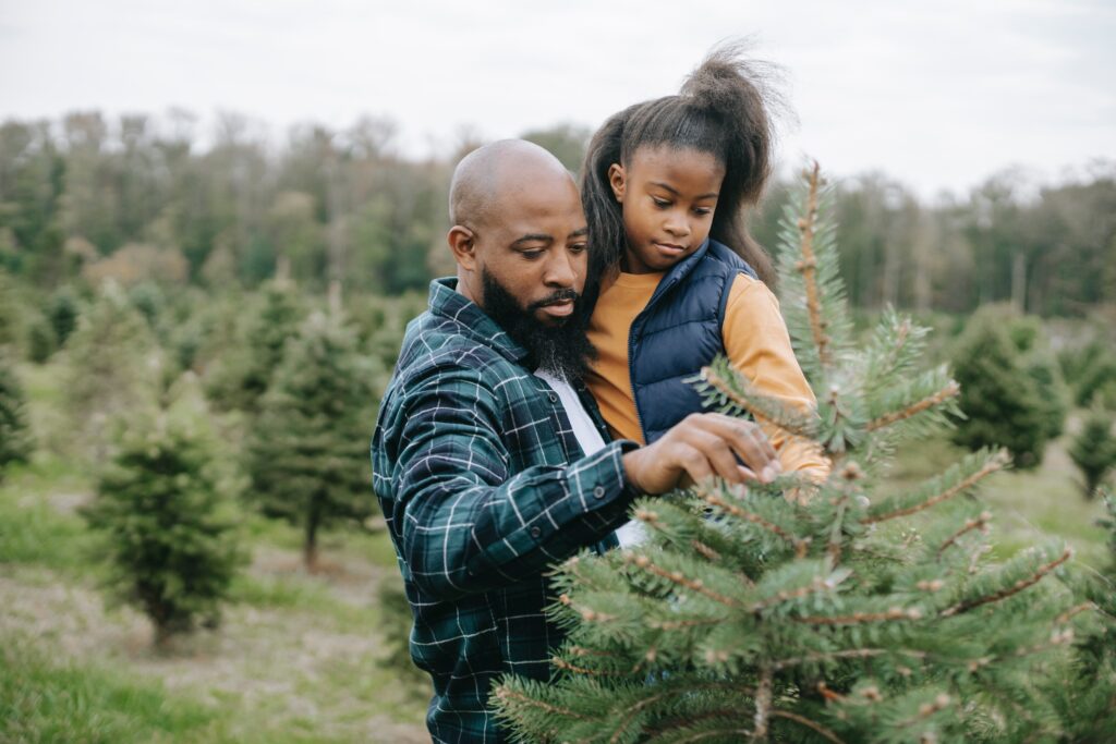man holding his daughter while the both inspect a Christmas tree