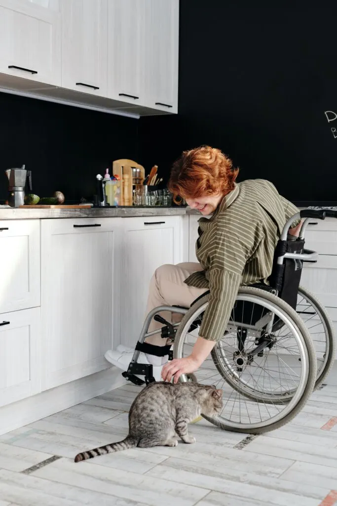 woman in wheelchair petting her cat in front of lowered countertops which is one way to make your home more handicap accessible