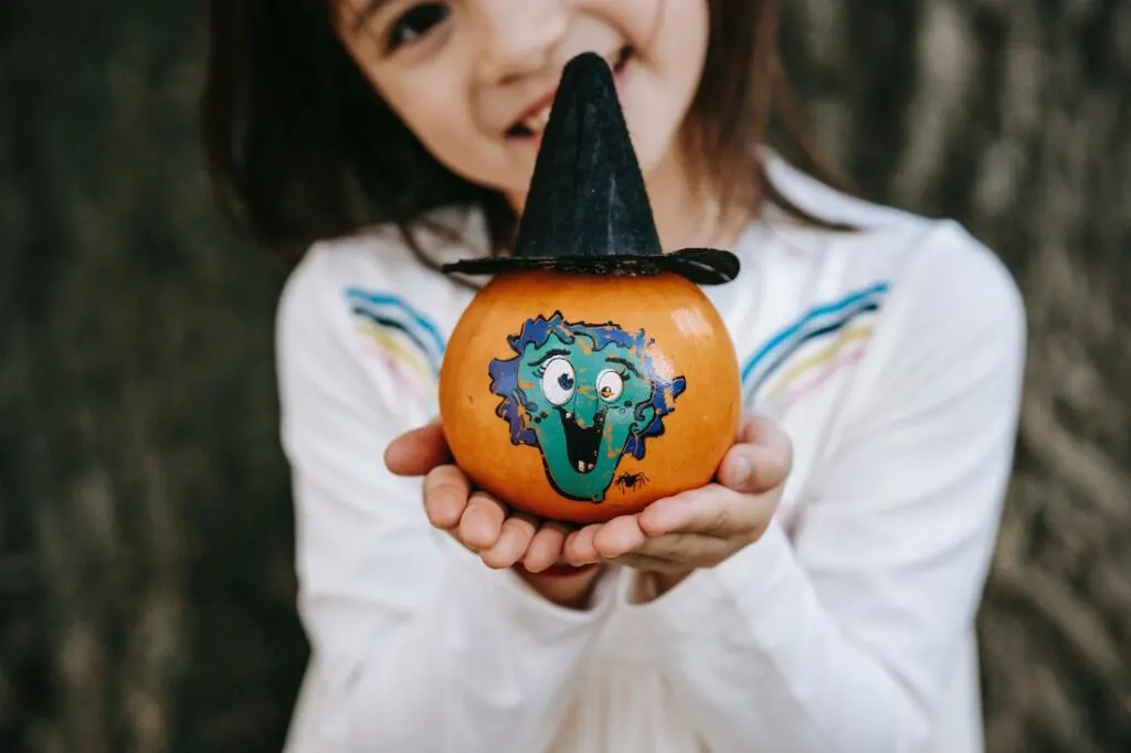 child holding a small pumpkin with a painted picture of a witch