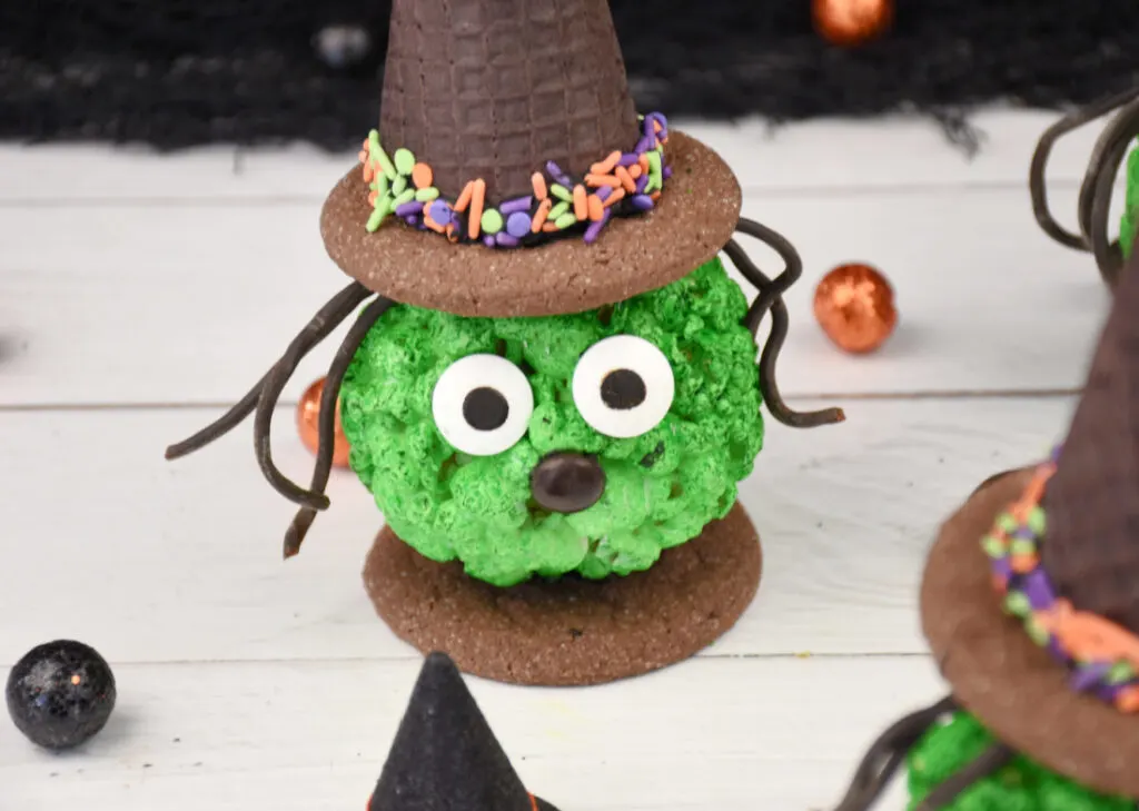 Halloween Popcorn Ball Witch made from a green popcorn ball and an ice cream cone and cookie hat, black licorice hair, and candy facial features.