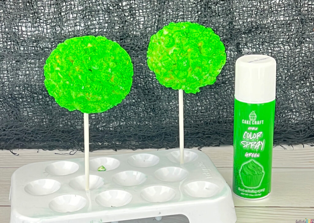 A Can of green Color Mist and two painted popcorn balls drying. 