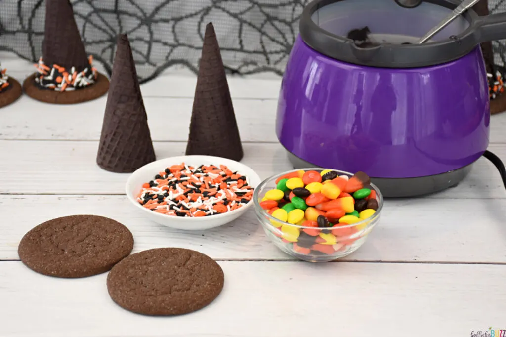 The melted candy melts in a purple candy melt machine along with other ingredients to make candy-filled witch hats laid out on a table
