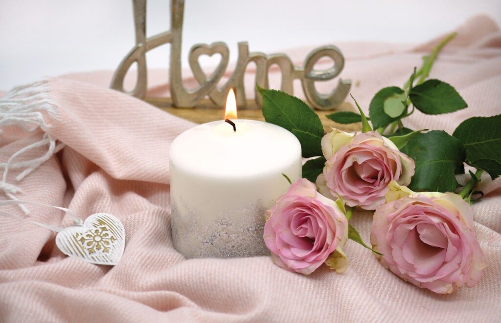 Home fragrance candle sitting on a pink blanket with pink roses laid next to it. Here are some tips on how to choose the perfect fragrance candle for every room
