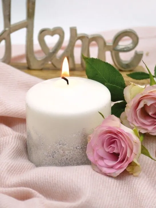 Home fragrance candle sitting on a pink blanket with pink roses laid next to it. Here are some tips on choosing the perfect fragrance candle for every room