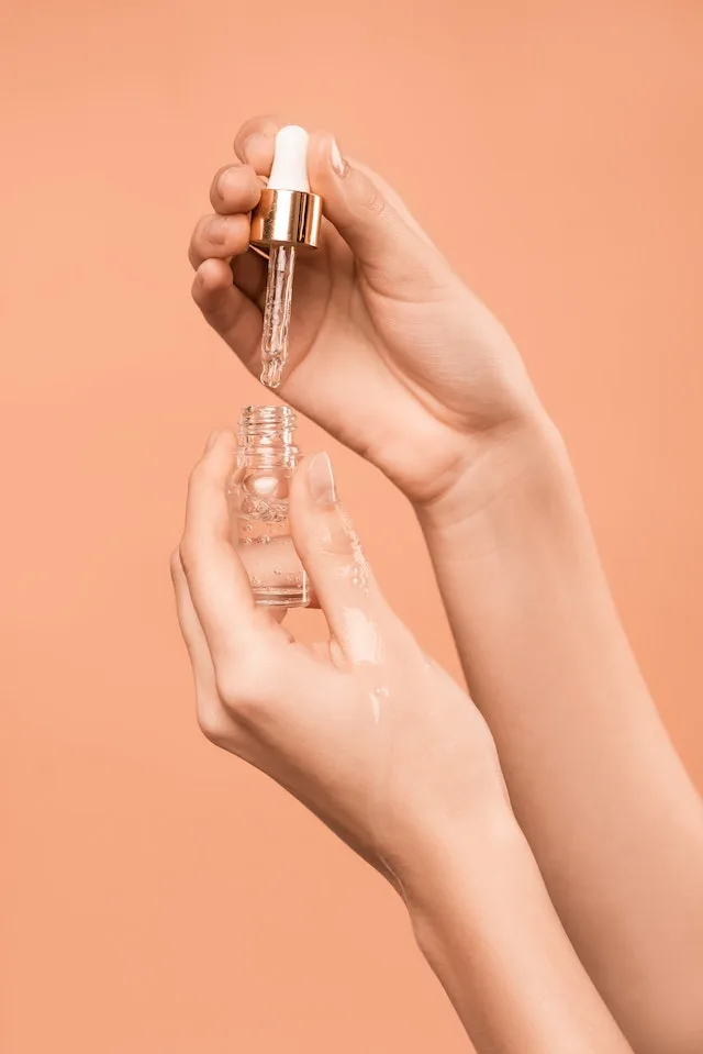 Woman holding a dropper above a bottle of serum.